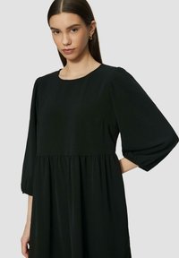 Schwarzes Kleid mit rundem Halsausschnitt, langen Puffärmeln und gestuftem Design, gefertigt aus einem leichten Stoff mit glatter Textur.