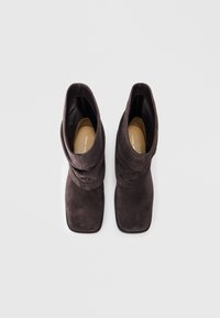 Botas de tobillo de ante marrón con un diseño arrugado, puntera cuadrada y un interior liso. Parte superior texturizada y suela de goma para mayor agarre.