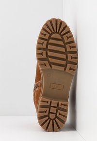 Botte en daim marron avec une semelle en caoutchouc texturé. Présente des coutures horizontales et un logo en relief sur la semelle. Taille 37 indiquée.