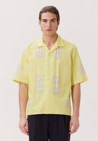 Camicia a maniche corte in tessuto giallo brillante con un motivo geometrico a catena grigia, con collo e chiusura a bottoni.