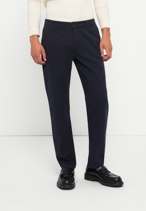Navy chinos made of cotton, featuring a straight-leg design, button closure, and side pockets. Worn with black slip-on shoes.