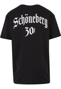 Sort bomulds T-shirt med korte ærmer, der har hvid gotisk stil tekst på ryggen, som læser "Schöneberg 30" og "Detshop."