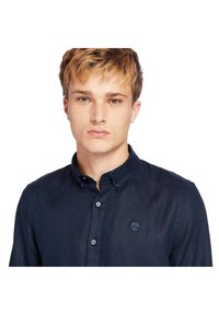 Camisa de botones navy hecha de una tela con una sutil textura, que presenta un cuello y un pequeño logo en el lado izquierdo del pecho.