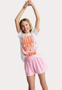 Witte T-shirt met grafische afbeelding van een oranje sardineblik en tekst, gecombineerd met roze gestreepte shorts. De outfit heeft een ontspannen pasvorm en een elastische tailleband.