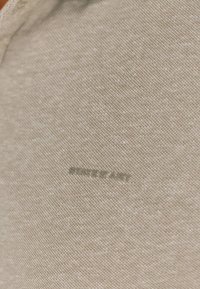 Beige stof met een fijne, gestructureerde weving; heeft een subtiel, geperst logo met de tekst "STATE OF ART" in een contrasterende kleur.