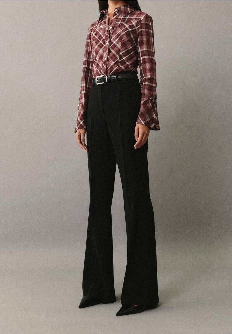 Červená károvaná košile na knoflíky s bílými akcenty, spárovaná s černými kalhotami s vysokým pasem, doplněná špičatými černými lodičkami.