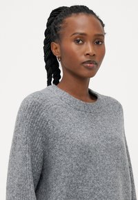 Maglione grigio lavorato a maglia con scollatura rotonda, caratterizzato da una finitura testurizzata e una leggera costina sui polsini, che conferisce un aspetto accogliente.