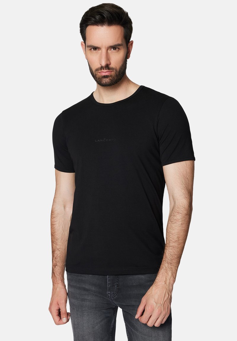 Czarna koszulka z okrągłym dekoltem, krótki rękaw, wykonana z miękkiego materiału, z delikatnym nadrukiem logo na środku, w zestawie z ciemnymi dżinsami.