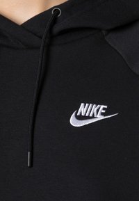 Svart huvtröja i mjukt tyg, med en vit broderad Nike-logga. Inkluderar snörning och texturerade axeldetaljer.