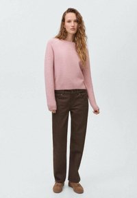 Suéter de punto de color rosa claro con mangas largas, combinado con pantalones de pierna ancha marrones y zapatos marrones. Diseño sencillo, textura suave.