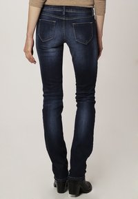 Vaqueros oscuros ajustados con un lavado desgastado, cinco bolsillos y detalles de costura sutiles, combinados con botas negras de tacón.