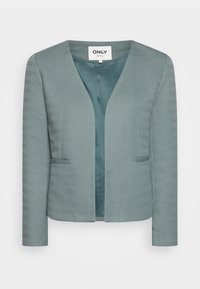 Blazer vert pâle texturé avec un col en V, ouverture frontale, manches longues et deux poches latérales. Motif chevrons ajoutant un détail subtil.