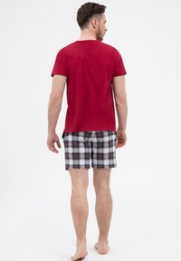 Czerwona koszulka z krótkim rękawem w połączeniu z czarno-białymi szortami w kratę, z różowymi akcentami. Materiał wydaje się gładki i lekki.