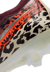 Gros plan du talon d'un crampon de football avec imprimé léopard, accents rouges et noirs, swoosh Nike argent métallique et semelle blanche translucide à crampons.