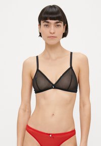 Črni prosojni modrček v obliki trikotnika z nežnim čipkastim robom, nastavljivimi naramnicami in detajlom s pentljo na sredini. Komplet dopolnjuje rdeč prosojen bikini spodnji del.