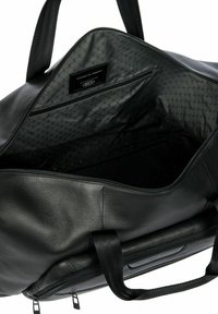 Sac de voyage en cuir noir avec surface texturée. Présente une doublure à motif hexagonal et une étiquette de marque à l'intérieur. Doubles poignées pour le transport.