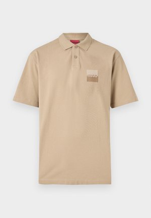 Bež polo majica s ovratnikom, tremi gumbi in žepom na prsih, ki nosi logotip "HUGO" v svetli barvi. Kratki rokavi.