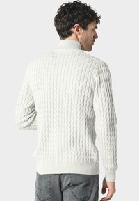 Maglione a maglia grossa color crema con colletto alto, polsini e orlo a coste, caratterizzato da una superficie testurizzata e un design in toni neutri.