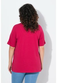 T-shirt fucsia a maniche corte con vestibilità ampia, scollo rotondo e texture liscia, abbinato a jeans azzurri chiari.