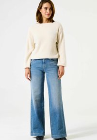 Pull en crème, duveteux et jean bleu clair évasé. Le pull a une coupe décontractée ; le jean présente une légère décoloration et un design classique à cinq poches.