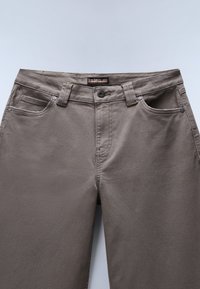 Γκρίζες βαμβακερές chinos με απαλή υφή. Διαθέτουν κλείσιμο με κουμπί, θηλιές ζώνης και μπροστινές τσέπες. Το λογότυπο της μάρκας είναι ορατό κοντά στη μέση.