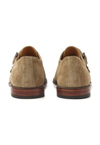 Brown suede shoes with a smooth texture, round toe, decorative buckle on the side, and a wooden base with a black rubber sole.
