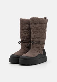 Botas marrones acolchadas con un acabado texturizado y puntera redonda, con una suela negra gruesa y un cordón ajustable en la parte superior.