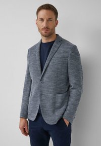 Grau strukturiertes Blazer mit maßgeschneidertem Schnitt, Reverskragen, einem Knopfverschluss und zwei Fronttaschen. Über einem dunklen Hemd getragen.