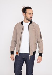 Bomberjack in lichtbeige, gemaakt van nylon, met een ritssluiting aan de voorkant, zwarte ribgebreide manchetten en een utility pocket op de mouw.