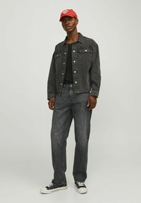 Hallide denim jakk, millel on ees taskud, must ribakät nong, hallid teksad ja mustad tossud. Punane müts, millel on valged tekstid, lisab värvi.