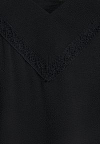 Mustat pusero, jossa on V-mallinen kaula-aukko, johon on lisätty monimutkainen pitsireunus. Kangas on pehmeä tekstuuri ja siinä on hieman kiiltoa.