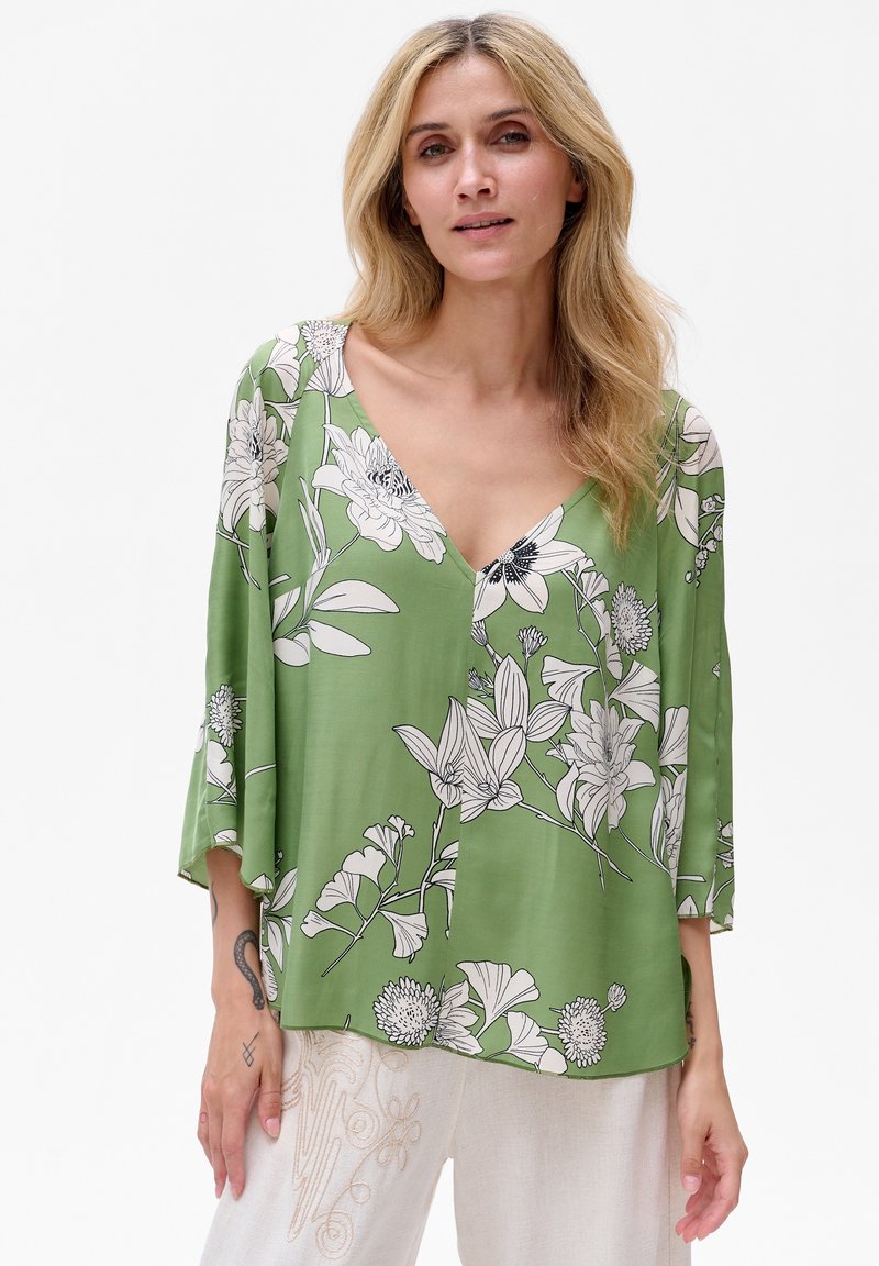 Zielona bluzka w kwiaty, wykonana z lekkiego materiału, z dekoltem w kształcie litery V, rękawami 3/4 oraz luźnym krojem, zdobiona czarno-białymi wzorami kwiatowymi.