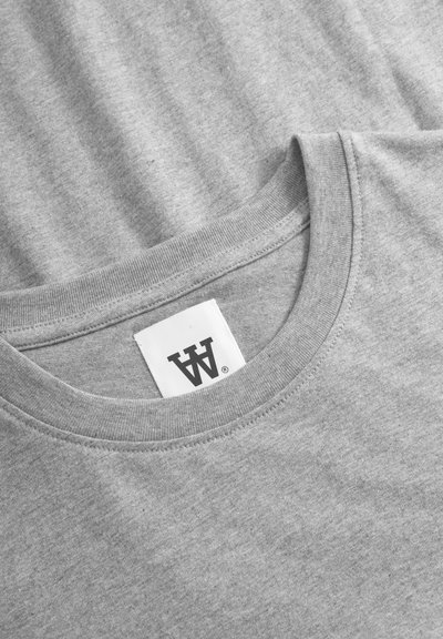 Tricou gri din bumbac, cu guler rotund, mâneci scurte și un etichetă cu un logo negru. Textura este netedă și ușor heathered.