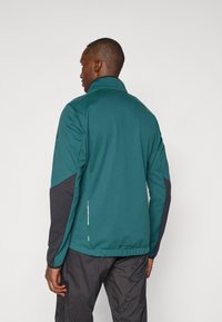 Türkisfarbene Softshelljacke mit schwarzen Akzenten, hohem Kragen, seitlichem Reißverschlusslicht, und verstellbarem Saum, aus einem leichten, strapazierfähigen Material.