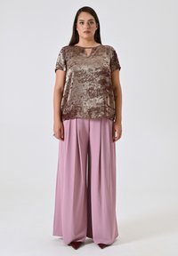 Top in bronzo metallico con maniche corte e scollatura a chiave, abbinato a pantaloni a gamba larga rosa chiaro a vita alta. Tessuto morbido, vestibilità comoda.