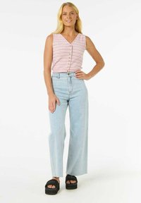 Top sans manches rayé rose et blanc avec des boutons, associé à un jean bleu clair à larges jambes et des sandales compensées noires. Fond blanc uni.