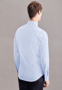 Camicia azzurro chiaro a maniche lunghe con colletto rialzato, piega sul retro e polsini con bottoni. Tessuto liscio e vestibilità su misura.