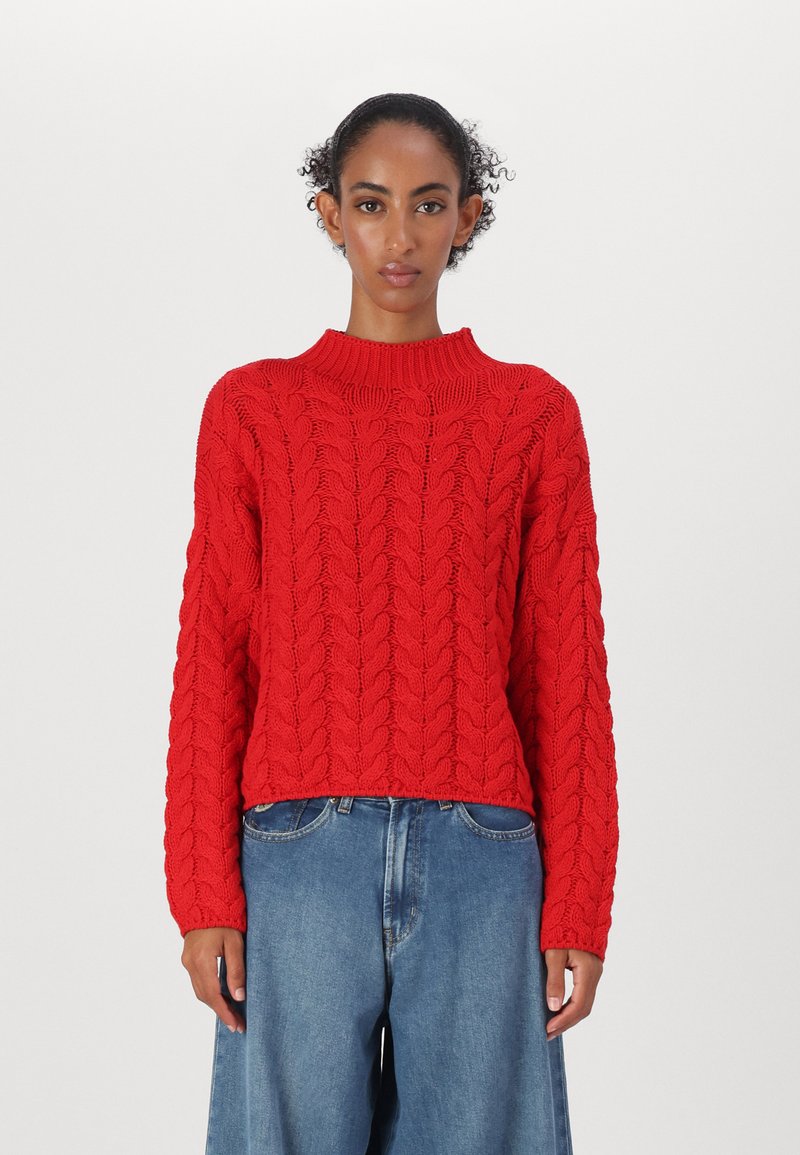 Rød cable-knit genser med høy krage og lange ermer, teksturert mønster, kort lengde, i kombinasjon med lyseblå løstsittende jeans.