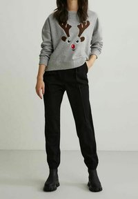 Sudadera gris con diseño de reno que presenta cuernos marrones y una nariz roja, acompañada de pantalones negros y botas negras hasta el tobillo.