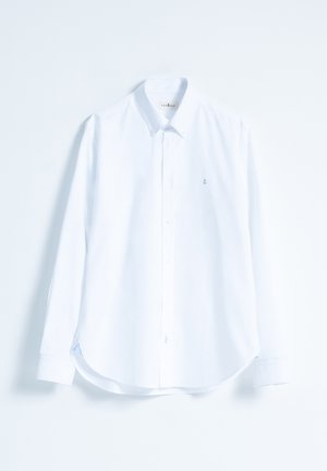 Camisa blanca de manga larga con cuello abotonado, hecha de algodón, presenta un logo sutil en el pecho y un dobladillo curvado con aberturas laterales.