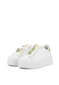 Sneaker bianchi con una piattaforma spessa, accenti dorati, decorati con gemme verdi sui lacci, caratterizzati da una texture in pelle liscia.