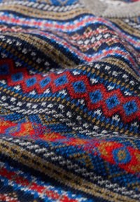 Megzta medžiaga su daugiaspalviu geometriniu raštu; rašto spalvos: raudona, mėlyna, auksinė ir balta prieš tamsų foną. Minkšta tekstūra, detalus dizainas.