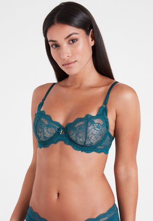 Teal lace bra with scalloped edges, underwire support, and decorative bow detail at the center. Adjustable straps and floral patterns.