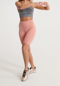 Ljust rosa högmidjade shorts i kombination med en grå kort sport-bh. Outfiten kompletteras av glittrande roséguldssportskor.