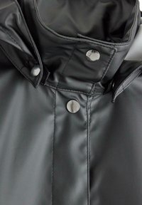 Collare di impermeabile nero, con una finitura liscia e lucida. Bottoni a pressione argentati e dettagli di cucitura accentuano il design.