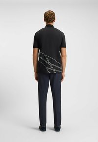 Czarna koszulka polo z krótkim rękawem, z białym geometrycznym wzorem z tyłu, w połączeniu z granatowymi spodniami i ciemnym obuwiem.