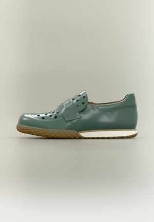 Baskets vertes brillantes avec perforations, bride en Velcro et semelle en caoutchouc marron texturée. Une semelle intermédiaire blanche borde le pourtour.