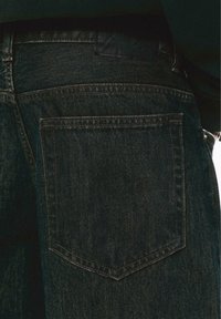Jeans in denim scuro con una singola tasca posteriore, caratterizzati da una sottile trama e cuciture a contrasto lungo i bordi.