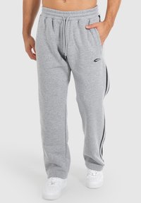 Graue Jogginghose mit einem Kordelzugbund, Seitentaschen und schwarzen Streifenakzenten an den Seiten. Hergestellt aus weichem, strukturiertem Stoff.