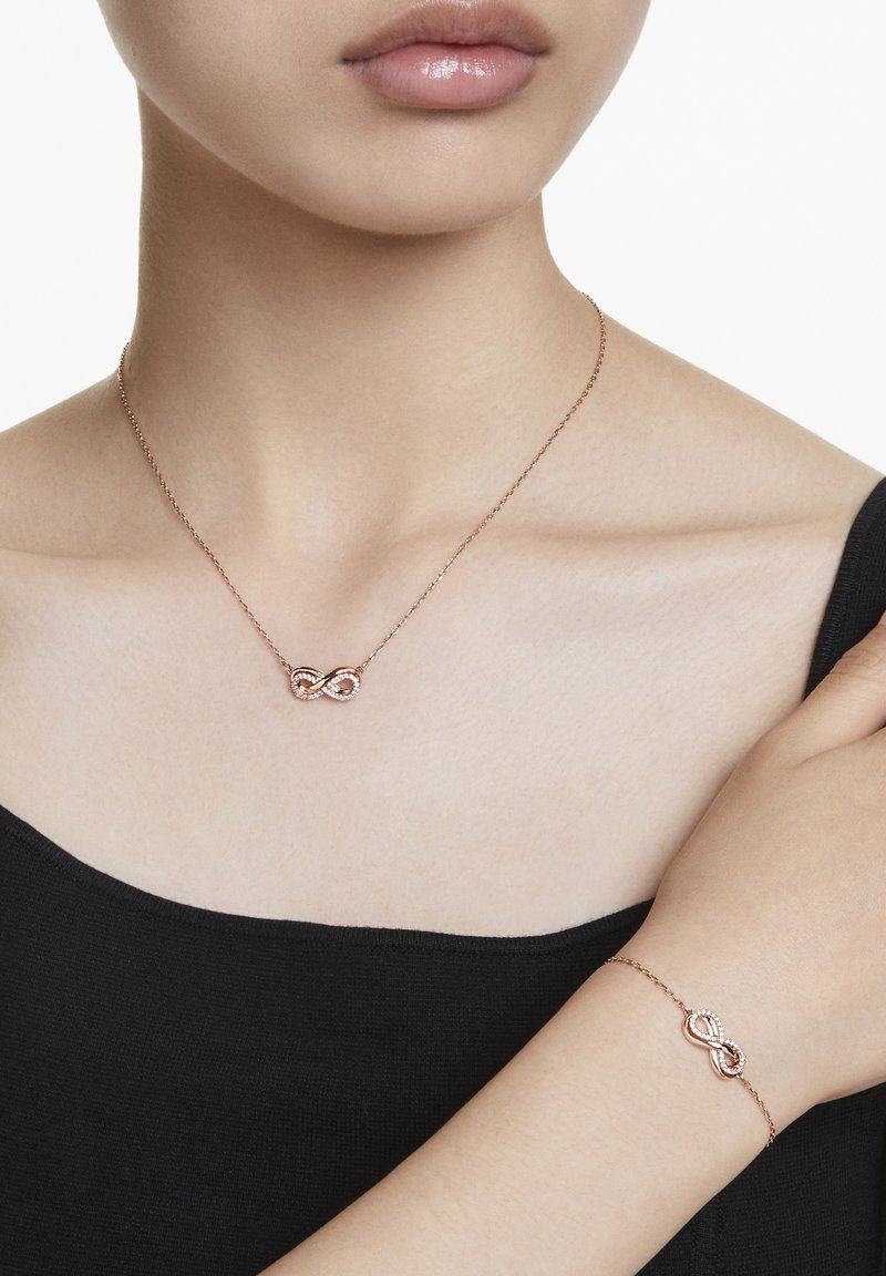 Halskette und Armband in roségold mit zarten Ketten, die ineinander verschlungene Unendlichkeitssymbole zeigen, besetzt mit kleinen klaren Steinen.